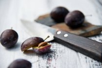 Damsons halved and whole with a knife on a rustic wooden surface — Stock Photo