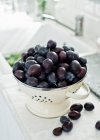 Fresh plums in vintage colander and on kitchen counter — Stock Photo