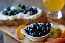 Kleine Schüssel mit Heidelbeeren und Pfirsichscheiben, Brotscheibe mit Ricotta und Blaubeeren auf dem Hintergrund — Stockfoto