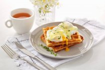 Waffle with dripping opened poached eggs with sauce and herbs — Stock Photo