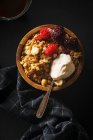 Granola con lamponi e more e un cucchiaio di panna in ciotola di legno con una tazza di caffè sul tavolo nero — Foto stock