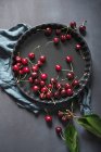 Cerezas dulces frescas en bandeja para hornear con paño y hojas verdes - foto de stock