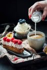 Eclair with berries and cream, and vanilla cupcake, pouring milk into coffee — Stock Photo