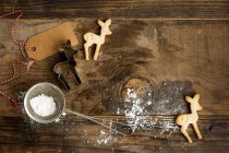 Biscuits festifs en forme de cerf de Noël sur une planche rustique avec coupe-biscuits, sucre glace au tamis et étiquette cadeau — Photo de stock