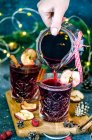 Chica vierte vino caliente de Navidad con manzanas secas de una jarra en vasos de cristal - foto de stock
