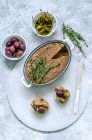 Liver pate in ceramic form, decorated with fresh thyme and two baguette sandwiches with pate, capers, olives on a marble stand — Stock Photo