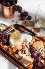 Cheeseboard with brie topped with honeycomb, crackers, walnuts, pistachios, grapes and white wine — Stock Photo