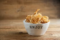 Dry fish and chips in bowl on wooden background — Stock Photo