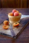 Apricots in wooden basket and on wooden board with knife — Stock Photo