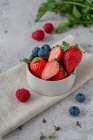 Erdbeeren, Blaubeeren und Himbeeren in kleinen Schälchen und auf dem Tisch — Stockfoto