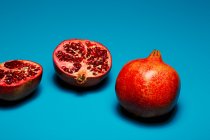 Whole and halved pomegranates on lush blue background — Stock Photo