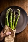 Hand holding a bundle of fresh green asparagus in a paper bag — Stock Photo