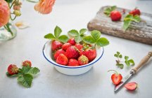 Fresh strawberries with green leaves in enamel bowl on wooden board — Stock Photo