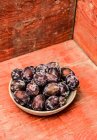 Fresh plums in bowl on red wooden surface — Stock Photo