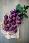 Fresh plums with green leaves with paper on wooden surface — Stock Photo