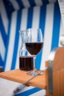 Una copa de vino tinto y una jarra de vino en una silla de playa - foto de stock