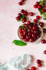 Fresh cherries with green leaves on pink surface with white cloth — Stock Photo