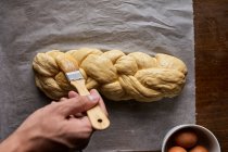 A braided loaf being spread with egg yolk — Stock Photo