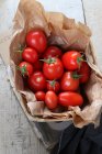 Свіжі помідори лози в паперовій сумці в дерев'яному кошику — стокове фото