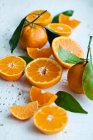 Naranjas con hojas enteras, cortadas a la mitad y rebanadas - foto de stock