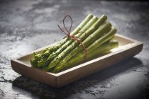 Un fascio di asparagi verdi in un piatto di legno — Foto stock
