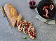 Sliced baguette topped with figs, goat's cheese and jam — Stock Photo