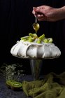 Main mettant sauce aux fruits avec cuillère sur pavlova gâteau décoré avec des tranches de kiwi — Photo de stock