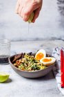 Hand squeezing lime on Thai broccoli rice with spicy dressing, eggs, and beef — Stock Photo