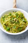 Спагетти со шпинатным песто, поджаренными кедровыми орехами и листьями базилика на сковороде — стоковое фото