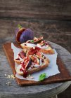 Baguette topped with figs and goat's cream cheese on wooden board — Stock Photo