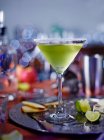 Appletini cocktail in martini glass with sugar, slices of apple and lime wedges with knife on metal tray — Stock Photo