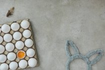 Ovos em recipiente de papel com ovo rachado e acessório de coelho da Páscoa — Fotografia de Stock