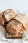 Two loaves of rye bread in paper bags on wooden board — Stock Photo