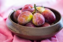Fresh plums in wooden bowl on pink cloth — Stock Photo