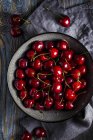 Sweet cherries in bowl on wooden table with cloth — Stock Photo