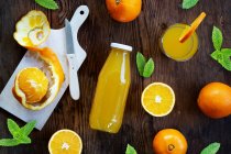 Jugo de naranja en un vaso y botella con naranjas frescas y hojas de menta - foto de stock