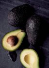 Avocados auf schwarzem Schiefer, eine halbiert — Stockfoto
