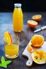 Suco de laranja em um copo e garrafa com laranjas frescas e folhas de hortelã — Fotografia de Stock