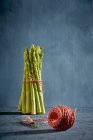Un paquet d'asperges vertes avec une boule de ficelle de cuisine au premier plan — Photo de stock