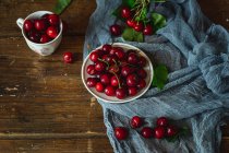 Fresh cherries with green leaves on cloth and on wooden table — Stock Photo