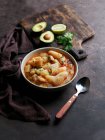 Bowl of potatoes with meat, avocado and lime with coriander on wooden board — Stock Photo