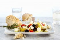 Сир Фета, що зберігається в оливковій олії з помідорами, часником, халапеносом та оливками, подається з прісним кунжутним хлібом — стокове фото
