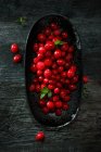 Cranberries frescos com folhas verdes na tigela e na mesa de madeira — Fotografia de Stock