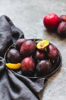 Fresh plums on plate with cloth on concrete surface — Stock Photo
