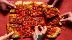 Roman style pizza topped with tomatoes and crushed red pepper flakes with hands — Stock Photo