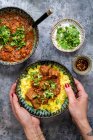 Mãos segurando prato de caril de carne com arroz de açafrão ao lado de tigelas — Fotografia de Stock