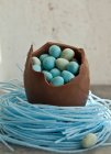 Большое шоколадное пасхальное яйцо, сидящее в гнезде черничных конфет, наполненное мини-шоколадными яйцами — стоковое фото