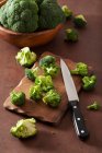 Fresh broccoli with a knife on a wooden chopping board and in a bowl — Stock Photo