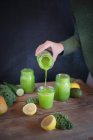 Una mujer vierte batidos verdes en vasos - foto de stock