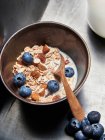 Bowl of muesli with raisins, almonds, blueberries and milk and wooden spoon — Stock Photo